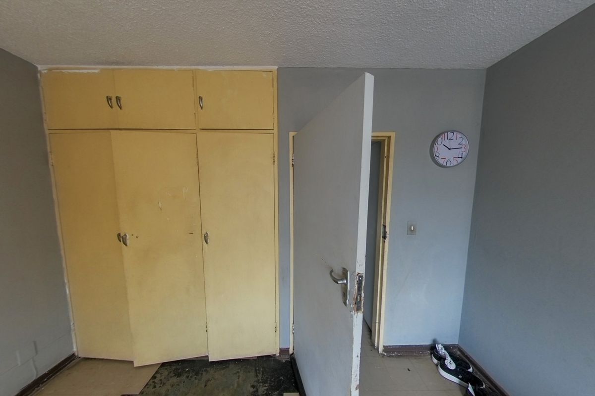 A bedroom featuring built-in cupboards with a neutral grey wall finish, requiring cosmetic updates to the flooring and cabinetry.
