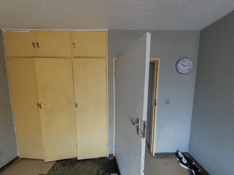 A bedroom featuring built-in cupboards with a neutral grey wall finish, requiring cosmetic updates to the flooring and cabinetry.