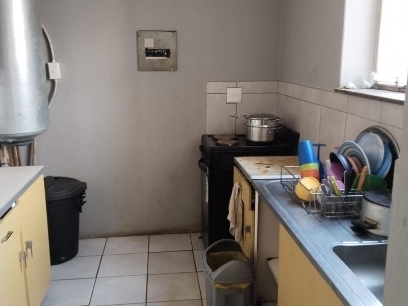 A functional kitchen featuring tiled flooring, built-in cabinetry, a stainless steel sink, and an electric stove, requiring cosmetic updates to improve its overall condition.