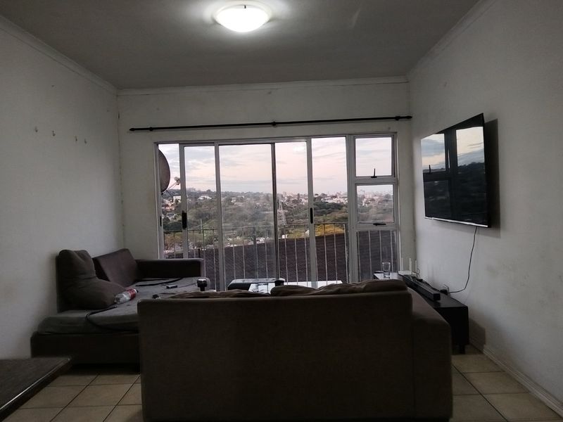 A living room featuring tiled flooring and large sliding glass doors that open to a balcony with an elevated urban view.