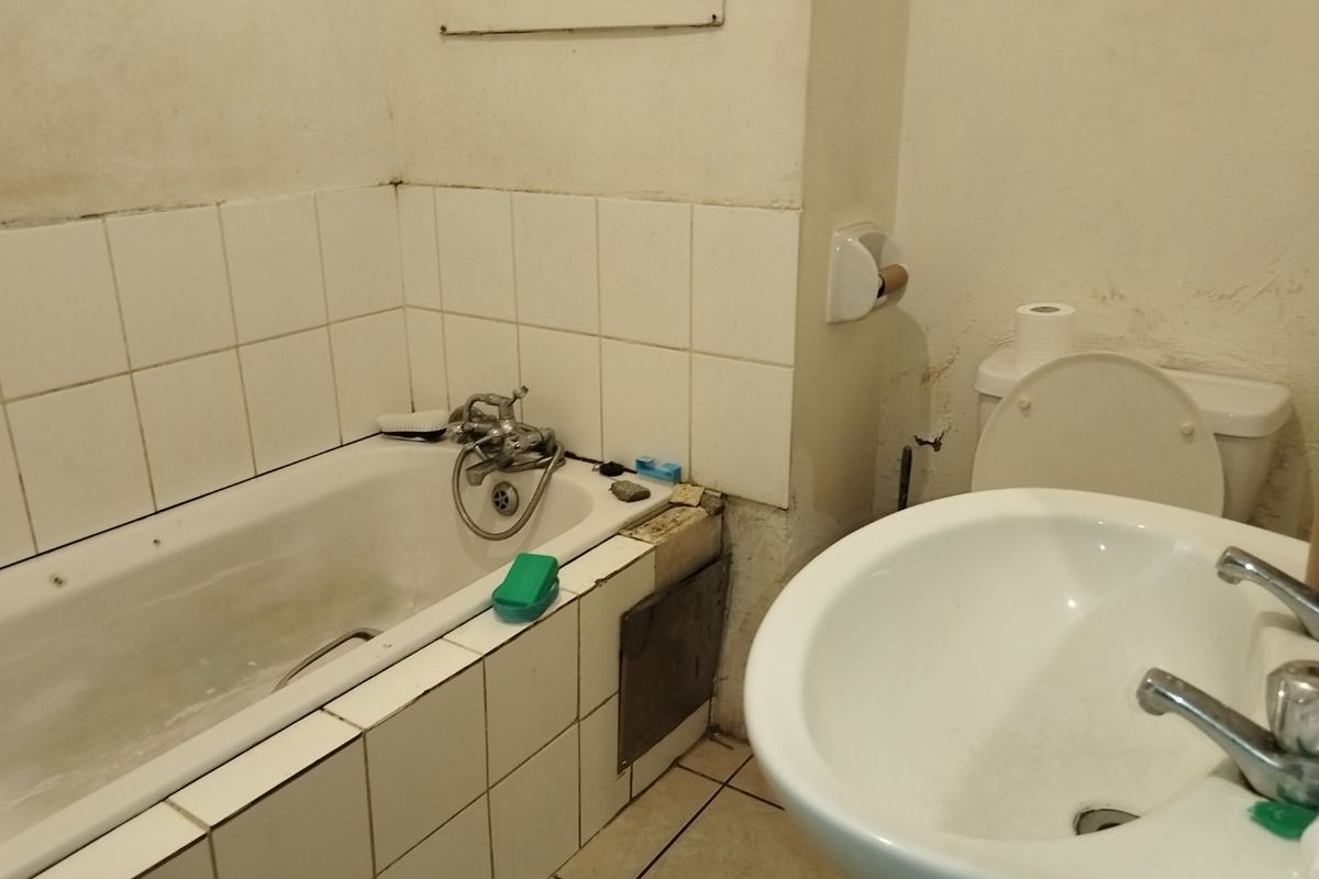 A dated bathroom featuring a bathtub, pedestal basin, and toilet, requiring significant maintenance and cosmetic updates to the wall finishes and fixtures.