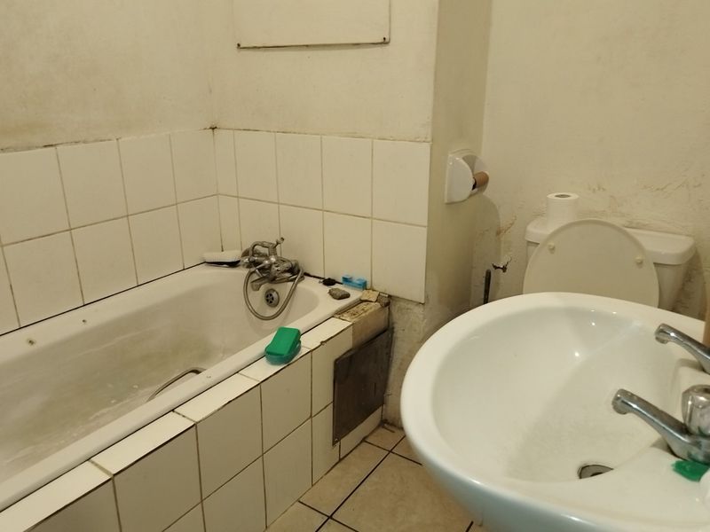 A dated bathroom featuring a bathtub, pedestal basin, and toilet, requiring significant maintenance and cosmetic updates to the wall finishes and fixtures.