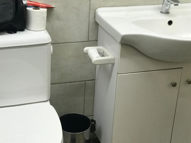 A functional bathroom featuring a white vanity cabinet with an integrated washbasin and a standard toilet against a tiled wall.
