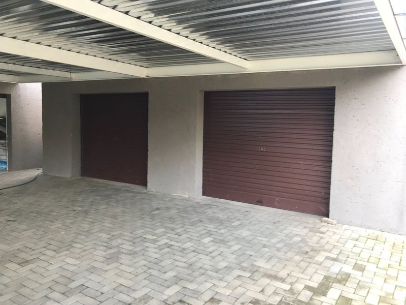 A functional double garage featuring secure roller shutter doors, a durable corrugated metal roof, and neat paved flooring.