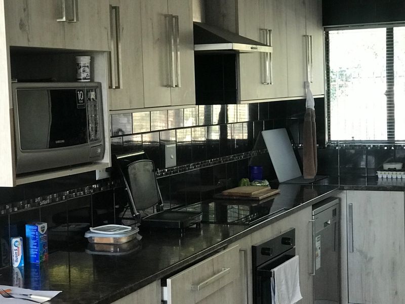 Modern kitchen featuring light wood-grain cabinetry, dark granite countertops, a black tiled backsplash, and integrated appliances including an oven and hob.