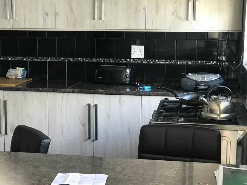 A functional kitchen featuring light wood-grain cabinetry, dark laminate countertops, and a contrasting black tiled backsplash with an integrated gas stove.