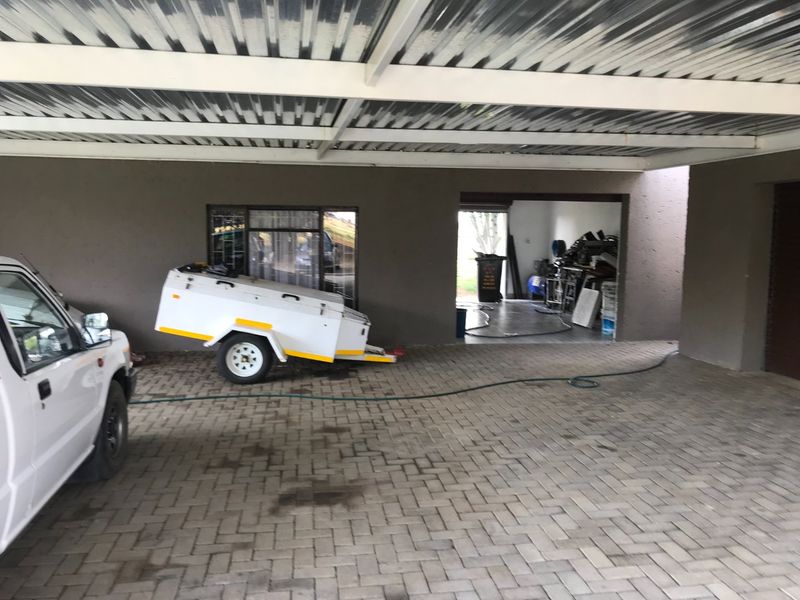 A covered carport area with paved flooring and corrugated metal roofing, providing sheltered parking space adjacent to a storage or utility area.
