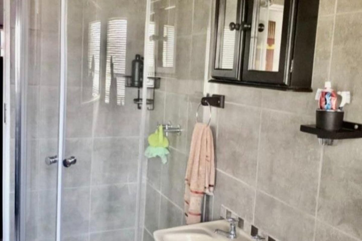A functional bathroom featuring a curved glass shower enclosure, pedestal basin, and neutral wall tiling with mosaic floor accents.
