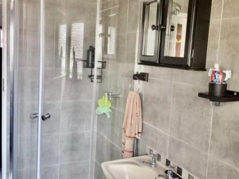 A functional bathroom featuring a curved glass shower enclosure, pedestal basin, and neutral wall tiling with mosaic floor accents.