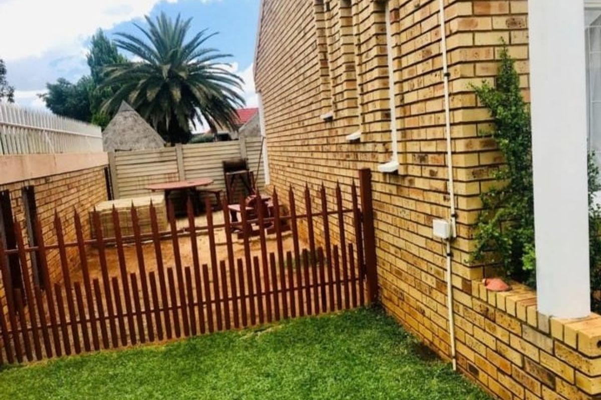 A side view of the townhouse featuring a face brick exterior, a small lawn area, and a fenced-off rear courtyard space.