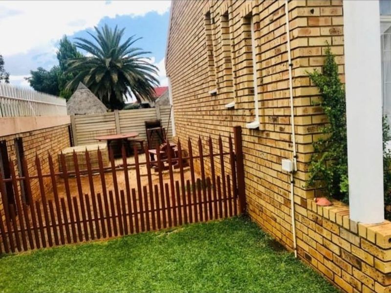A side view of the townhouse featuring a face brick exterior, a small lawn area, and a fenced-off rear courtyard space.