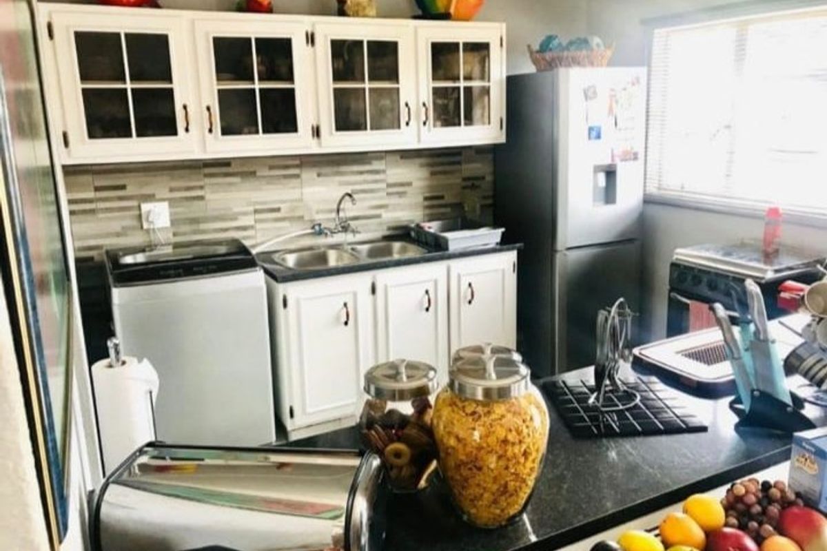 A functional kitchen featuring white cabinetry, a double sink, tiled backsplash, and a dark countertop, providing a practical workspace for daily meal preparation.