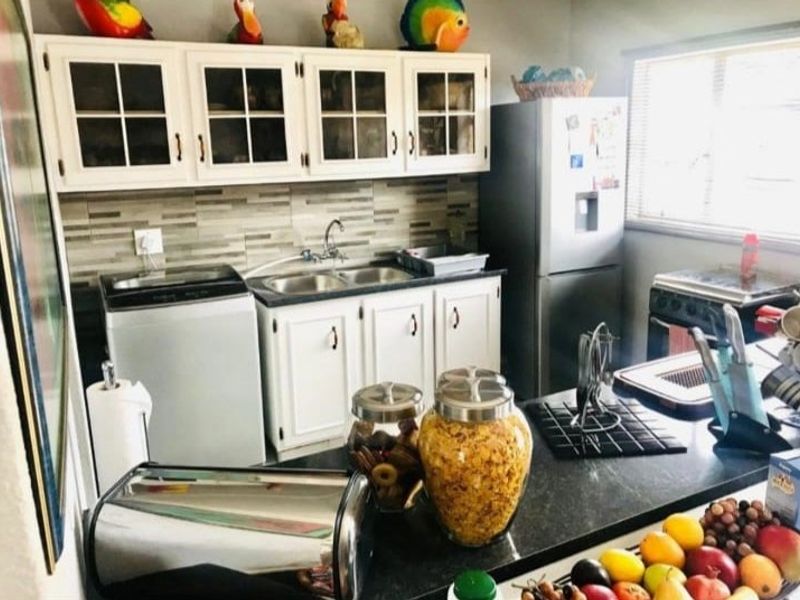 A functional kitchen featuring white cabinetry, a double sink, tiled backsplash, and a dark countertop, providing a practical workspace for daily meal preparation.