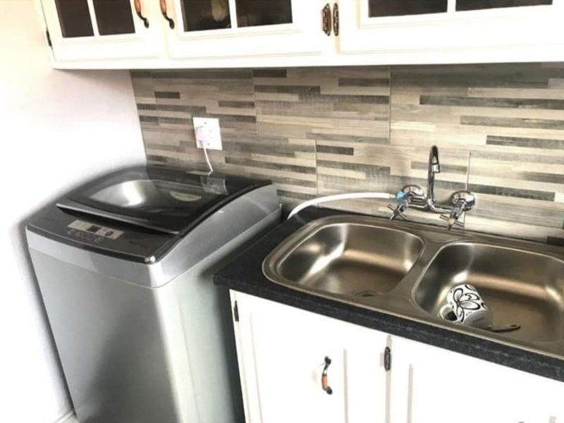 A functional laundry area featuring a double stainless steel sink, tiled backsplash, and ample upper and lower cabinetry for storage.