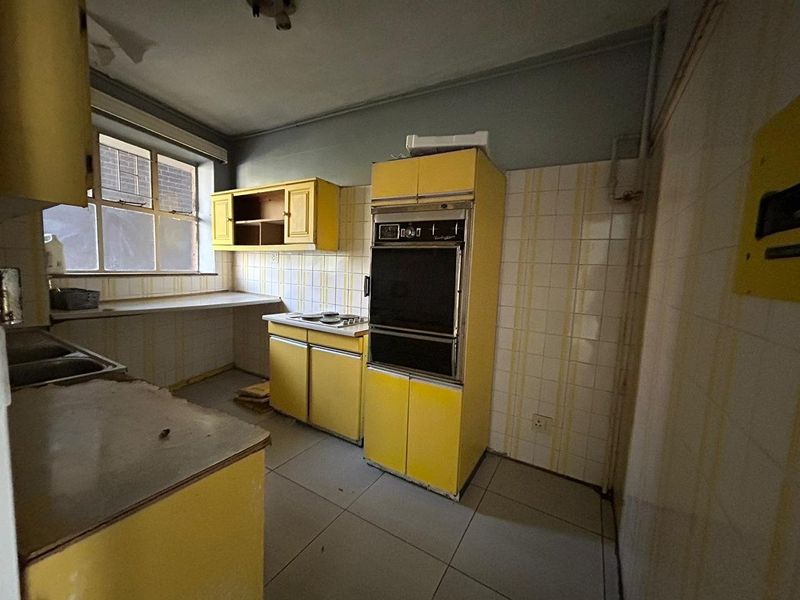 A dated kitchen featuring original yellow cabinetry, built-in oven, cooktop, and tiled surfaces, requiring significant renovation to modernize the space.