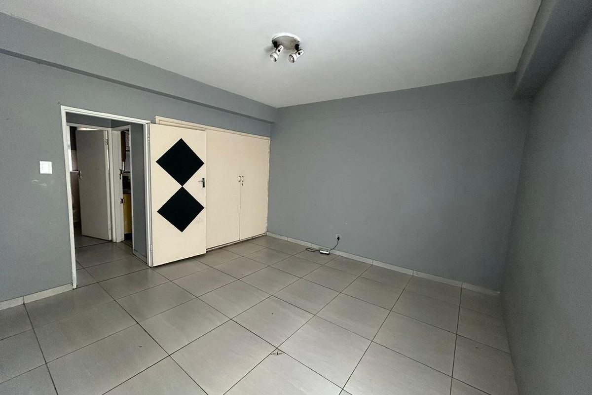 An empty bedroom featuring neutral grey walls, tiled flooring, and built-in storage cupboards.