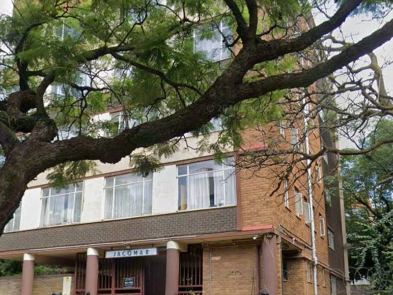 Front elevation of the Jacomar apartment building featuring a brick facade, secure metal fencing, and gated entrance.