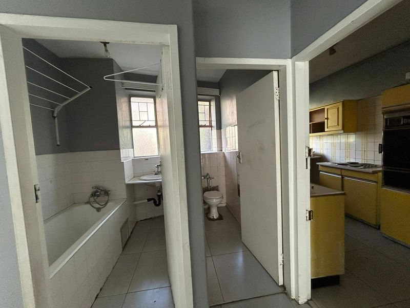 A view from the hallway looking into a bathroom, separate toilet, and dated kitchen with original cabinetry and built-in appliances.