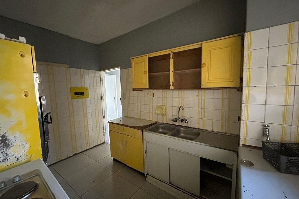 A dated kitchen featuring original cabinetry, a double basin sink, and tiled backsplash, requiring significant renovation to modernize the space.
