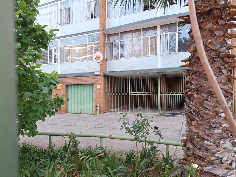 Front elevation of an apartment building featuring brick facade, ground-level garage access, and secure metal gated parking area.
