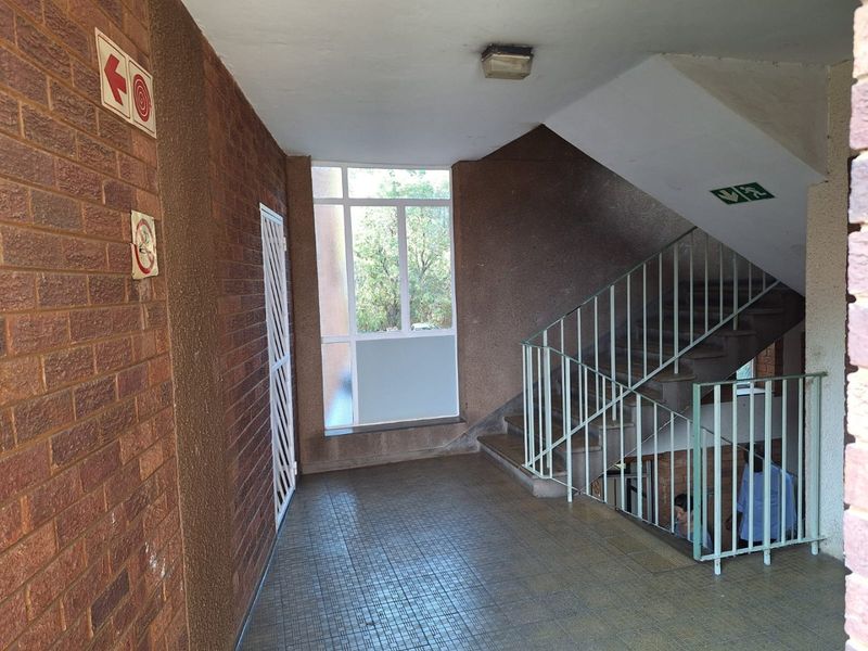 A communal apartment hallway featuring a staircase with metal balustrades, tiled flooring, and exposed brick walls.