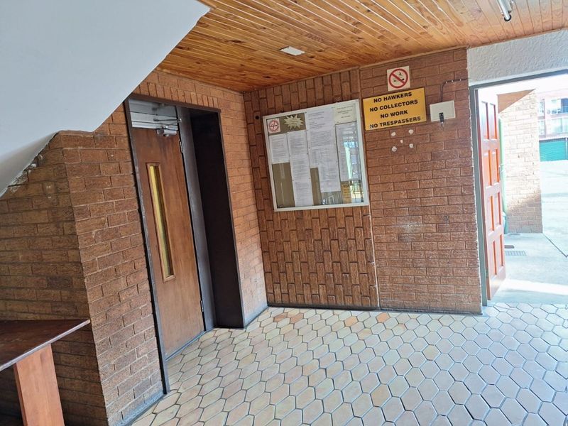 A functional apartment building entrance lobby featuring exposed brick walls, timber ceiling paneling, and tiled flooring.