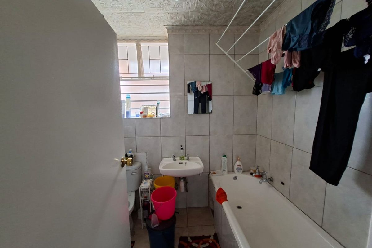 A functional bathroom featuring a bathtub, wall-mounted basin, and toilet, with tiled finishes throughout and a textured ceiling.