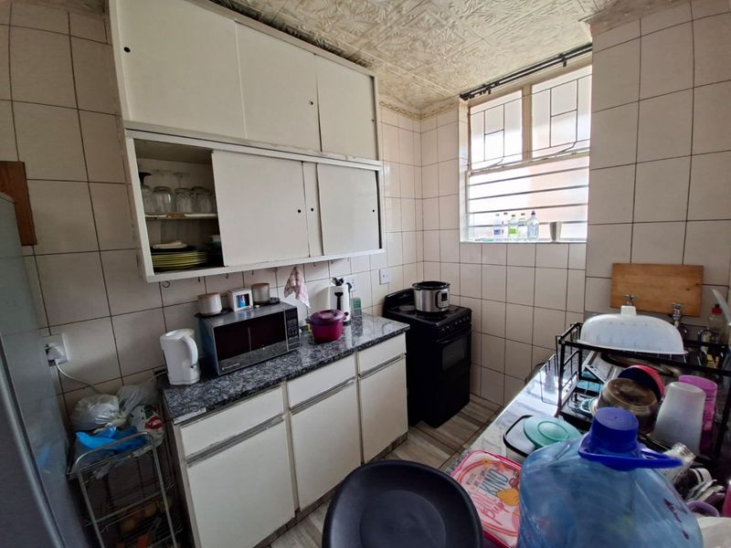 A compact kitchen featuring dated cabinetry, tiled walls, and a freestanding stove, offering potential for a modern renovation.