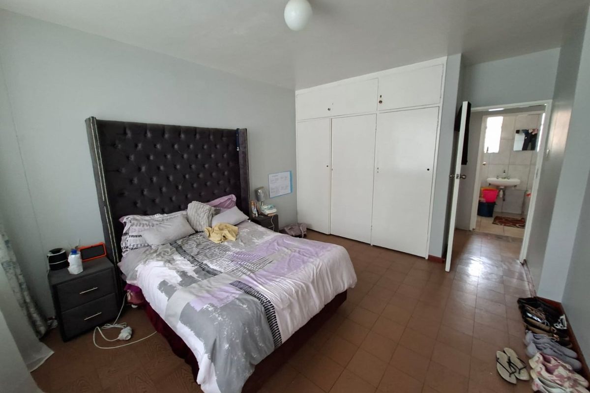 A bedroom featuring built-in cupboards, tiled flooring, and an en-suite bathroom access, offering a functional space with potential for cosmetic updates.
