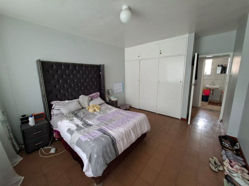 A bedroom featuring built-in cupboards, tiled flooring, and an en-suite bathroom access, offering a functional space with potential for cosmetic updates.