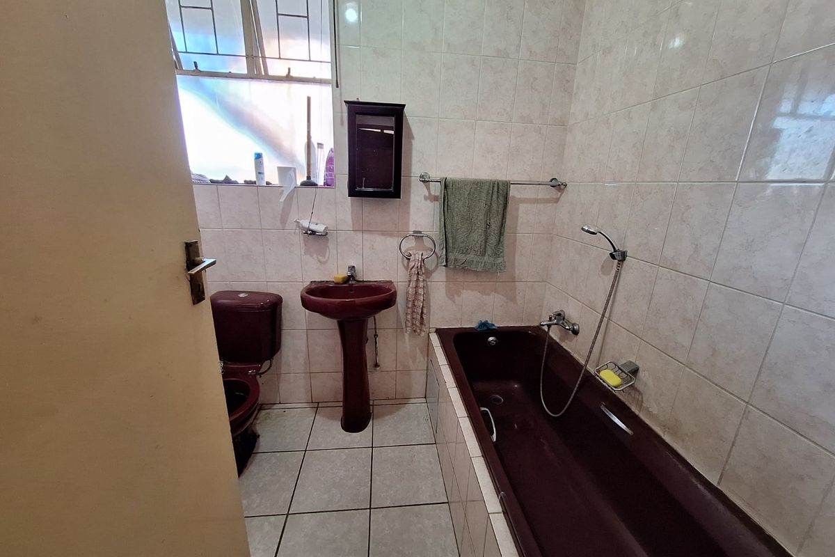 A dated bathroom featuring a dark-toned pedestal basin, bathtub, and toilet with neutral wall and floor tiling.