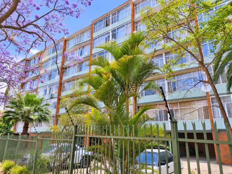 Exterior view of a multi-story apartment building featuring a brick and glass facade with secure perimeter fencing.