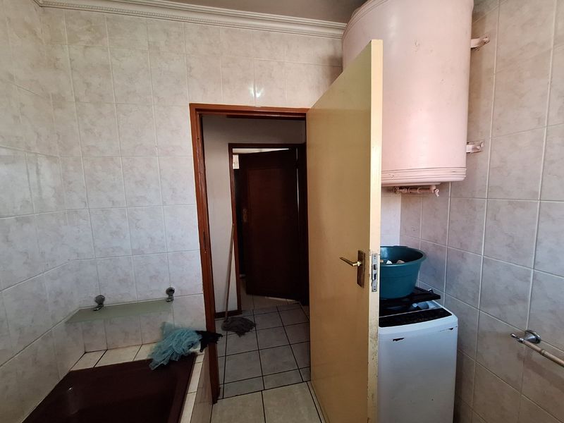 A functional laundry area featuring ceramic wall and floor tiling, a wall-mounted electric water heater, and direct access to the hallway.