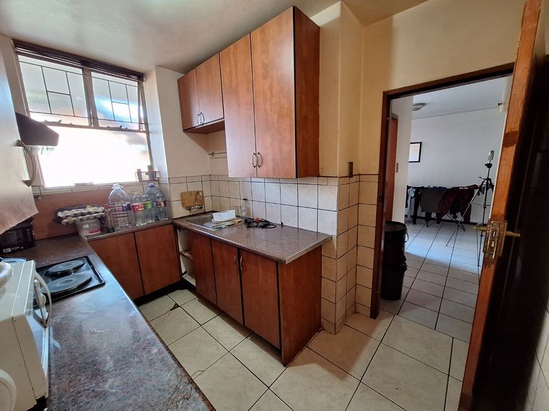 A compact kitchen featuring laminate cabinetry, granite-look countertops, a stainless steel sink, and ceramic tile flooring, offering a functional layout with potential for modernization.