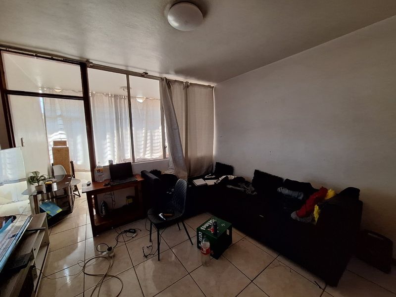 A living room area featuring tiled flooring and a large glass sliding door leading to an adjacent space, providing natural light.