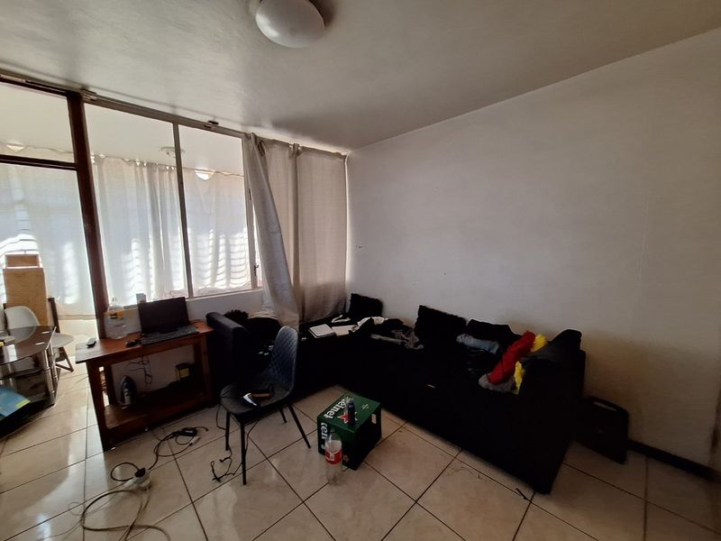 A living room area featuring tiled flooring and a large sliding glass door providing natural light, with potential for cosmetic updates.