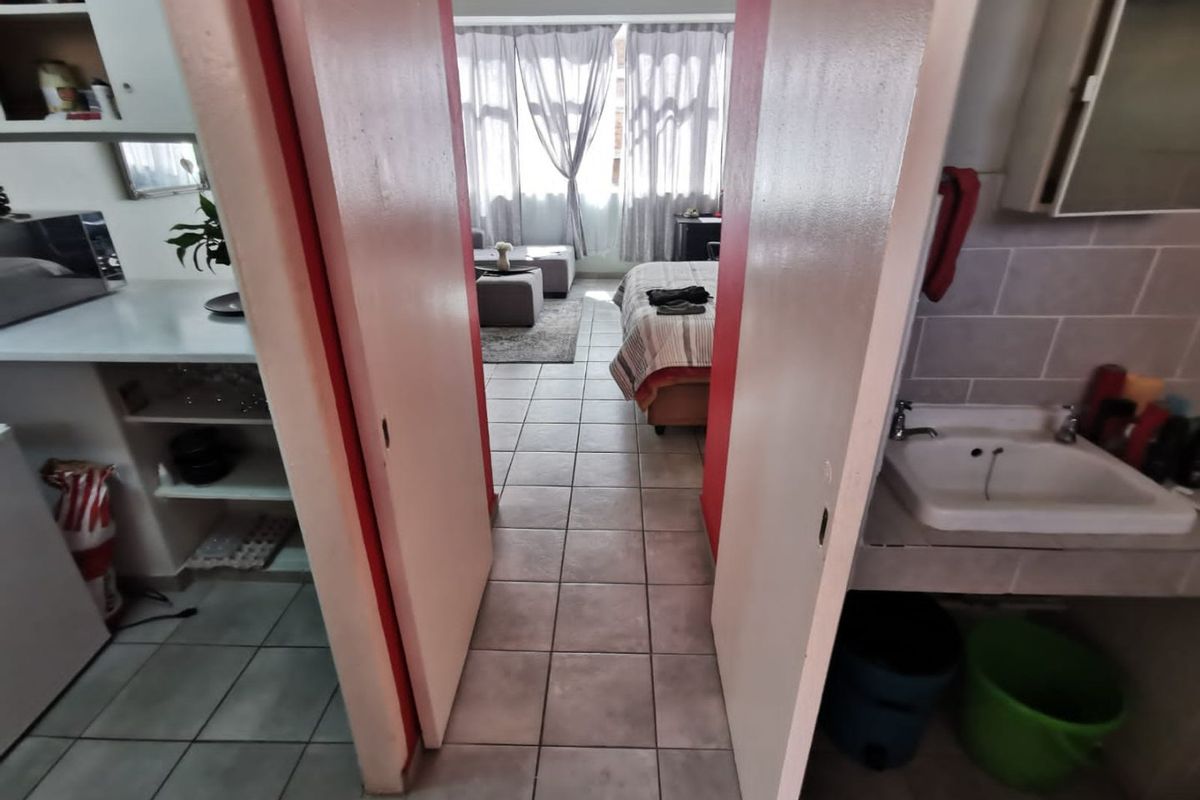 Open plan apartment layout featuring tiled flooring, a built-in bathroom vanity, and kitchen cabinetry, connecting the living and sleeping areas.
