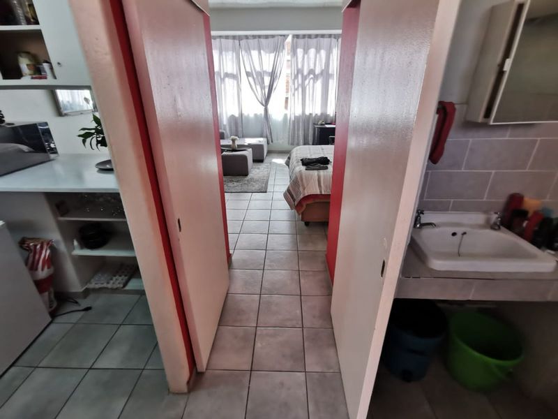 Open plan apartment layout featuring tiled flooring, a built-in bathroom vanity, and kitchen cabinetry, connecting the living and sleeping areas.