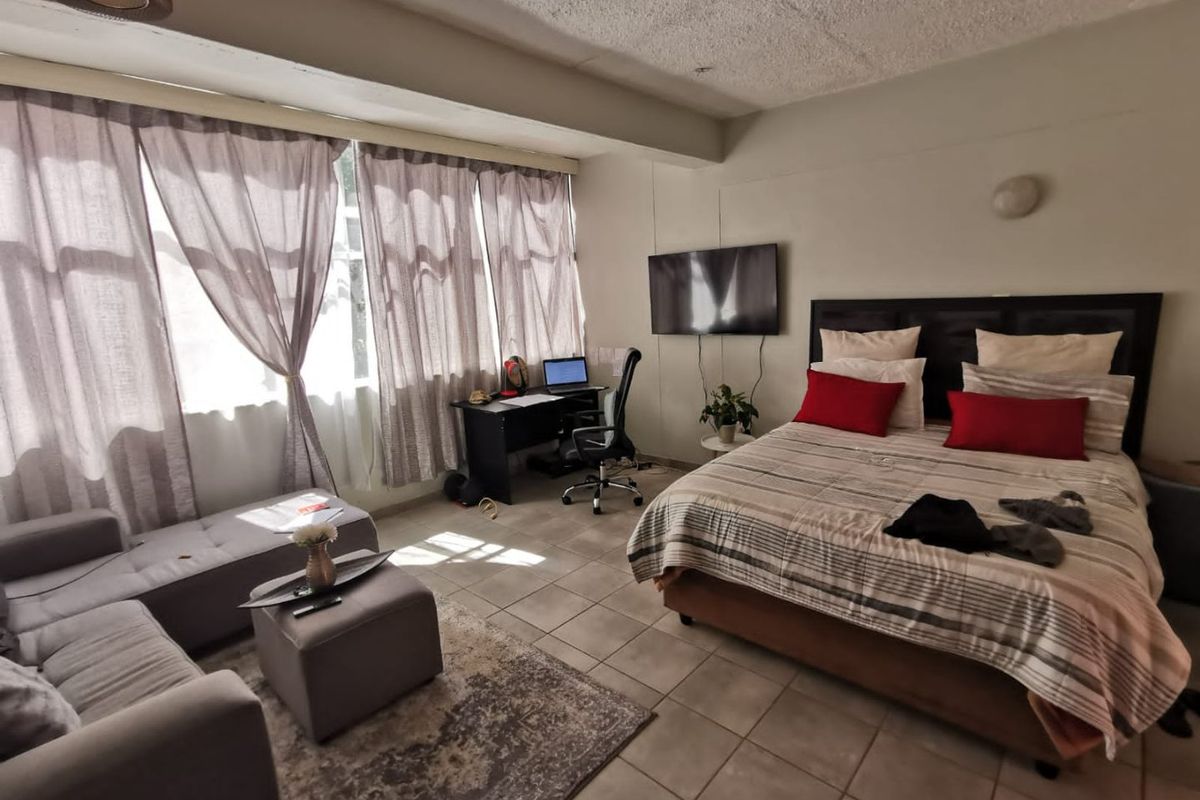 Spacious bedroom featuring tiled flooring, a textured ceiling, and a wall-mounted television, offering a functional layout with ample natural light.
