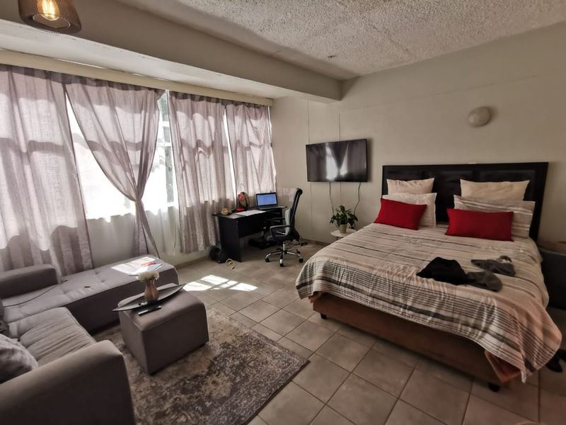 Spacious bedroom featuring tiled flooring, a textured ceiling, and a wall-mounted television, offering a functional layout with ample natural light.
