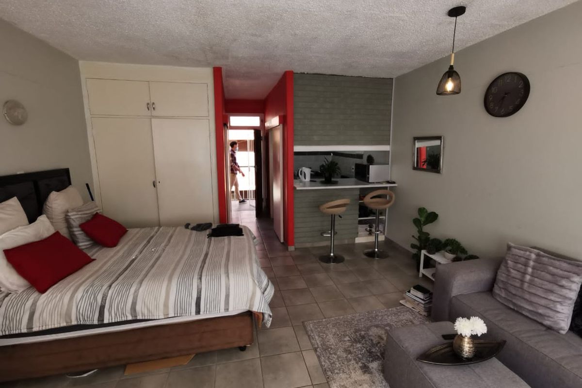 Open-plan studio apartment featuring a combined bedroom and living area with a compact breakfast bar kitchen and built-in storage cupboards.