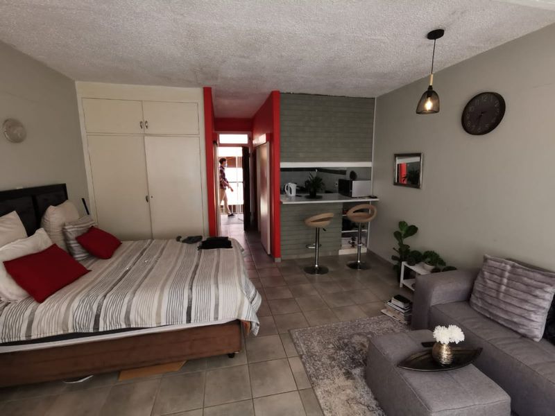 Open-plan studio apartment featuring a combined bedroom and living area with a compact breakfast bar kitchen and built-in storage cupboards.