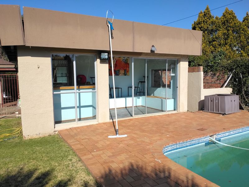 Outdoor pool area featuring a brick paved patio, swimming pool, and a structure with sliding glass doors and a built-in bar.