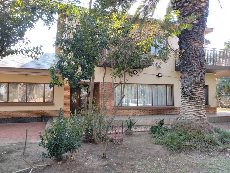 Rear view of the house featuring a brick facade, a balcony with metal railings, and a paved patio area surrounded by mature garden landscaping.