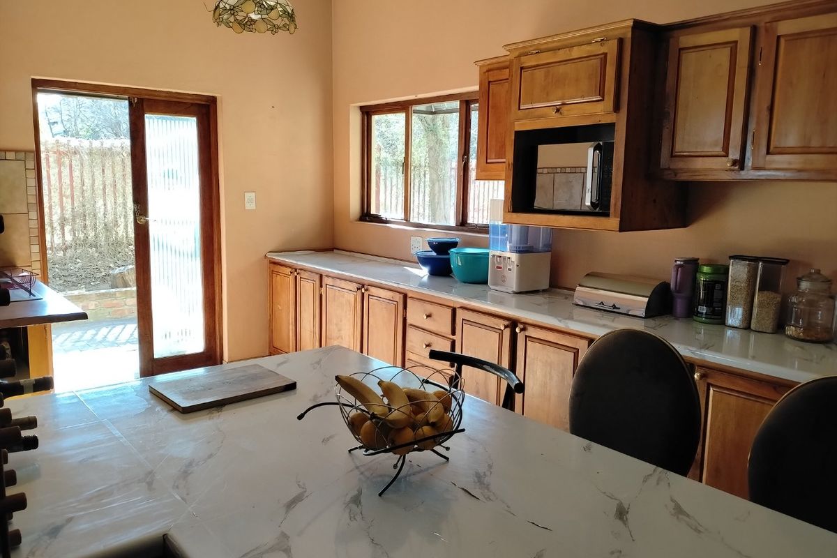 A functional kitchen featuring wooden cabinetry, marble-effect countertops, and direct access to the outdoor area through a sliding glass door.