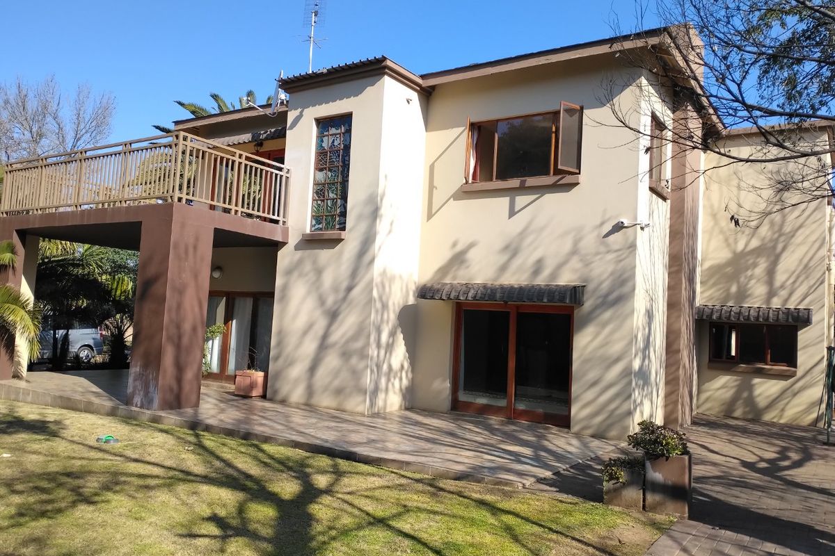 Rear view of a two-story house featuring a tiled patio, a spacious upper-level balcony with metal railings, and sliding glass door access.