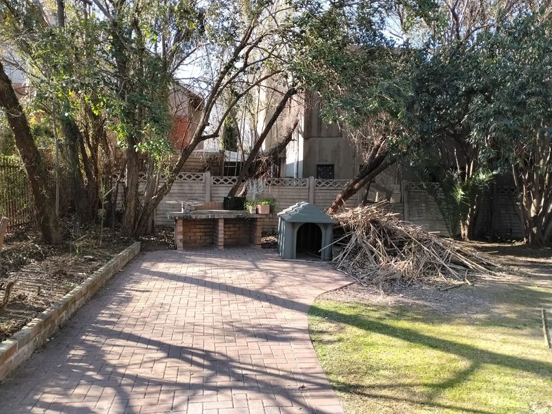 Rear garden area featuring a brick paved patio, built-in brick braai, and precast boundary wall, requiring landscaping and clearing of debris.