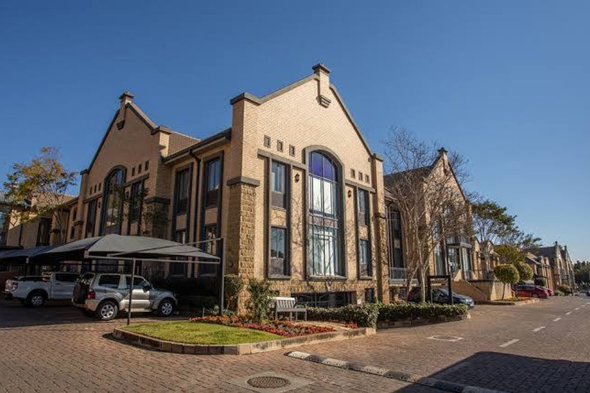 A professional exterior view of a multi-story commercial brick building featuring arched windows, paved parking areas, and covered carport structures.
