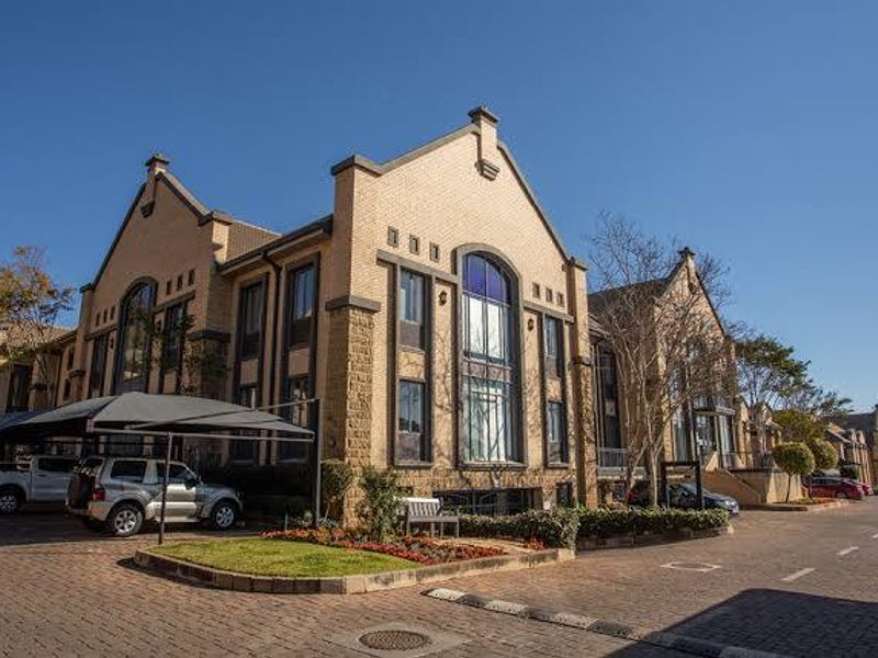 A professional exterior view of a multi-story commercial brick building featuring arched windows, paved parking areas, and covered carport structures.