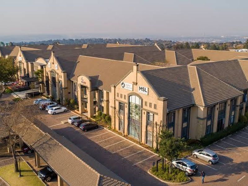 Aerial view of a commercial office complex featuring tiled roofing, extensive paved parking, and covered parking bays.